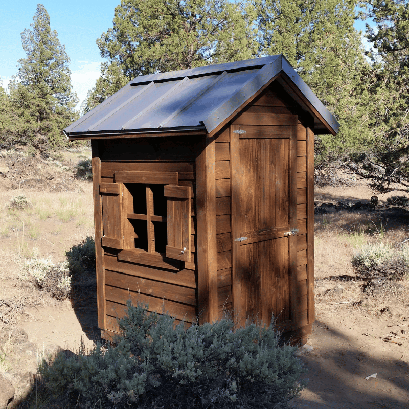 Oregon Timber Werks handmade rustic wooden outhouse cabin nestled in the forest with an open window, showcasing the natural surroundings and eco-friendly craftsmanship